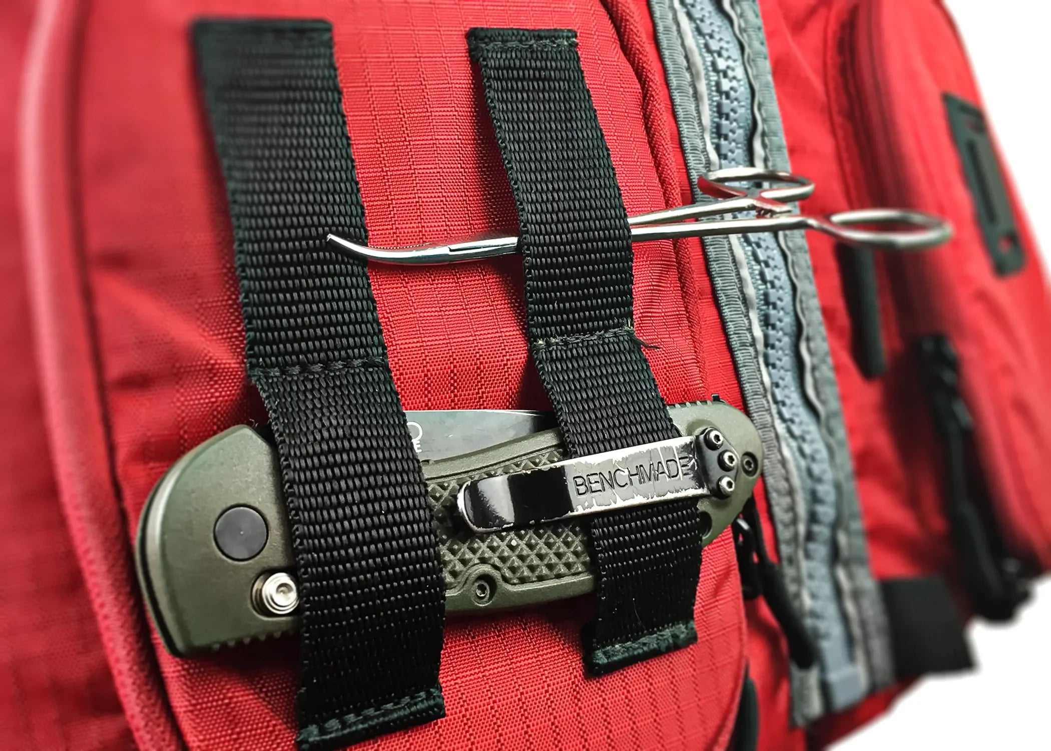 Close-up of Stohlquist red kayaking life jacket with black straps securing a folding knife and hemostat tool.