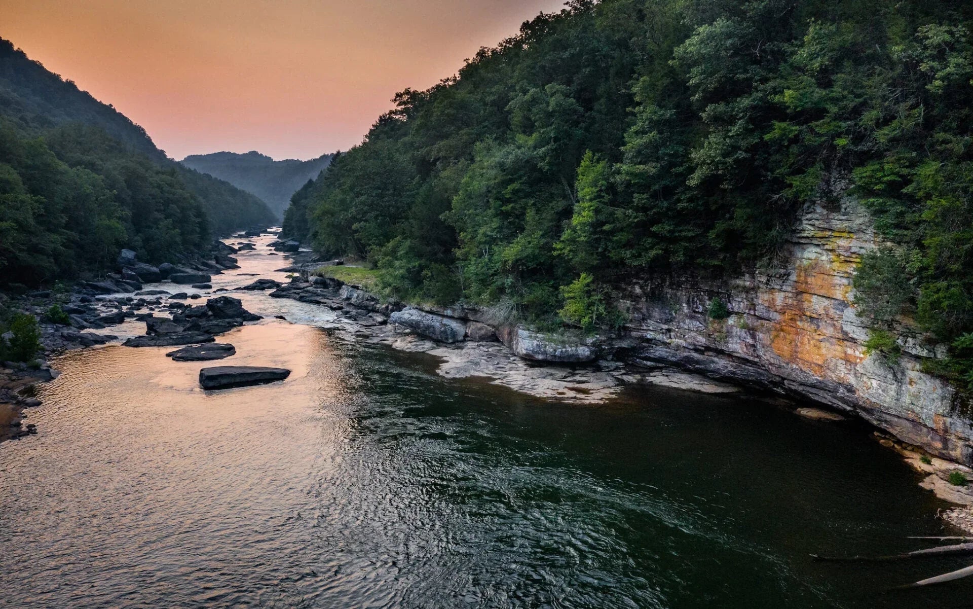 Scenic river flowing between forested cliffs at sunset, ideal for kayaking and paddling adventure