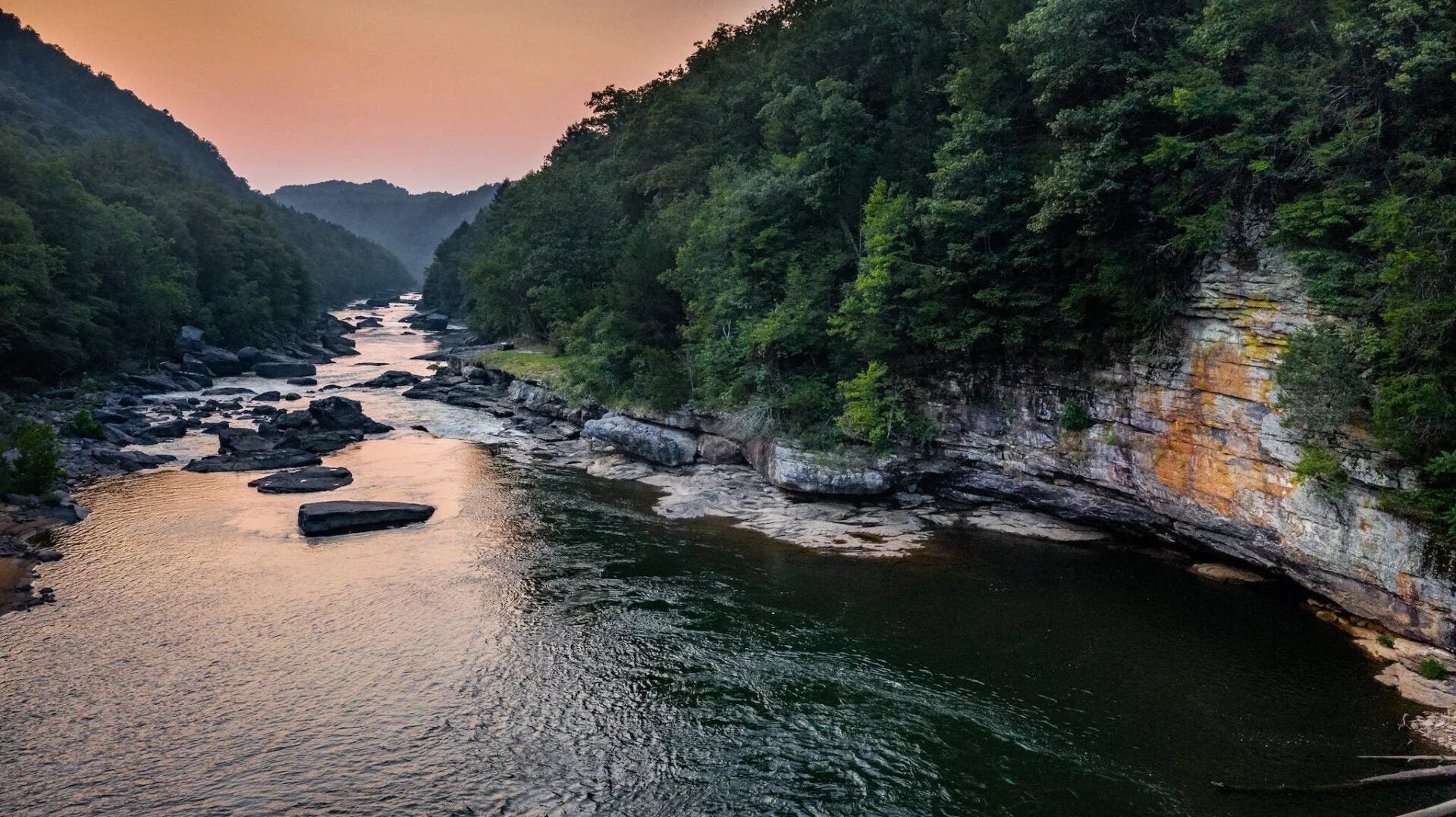 Scenic river flowing between forested cliffs at sunset, ideal for kayaking and paddling adventure