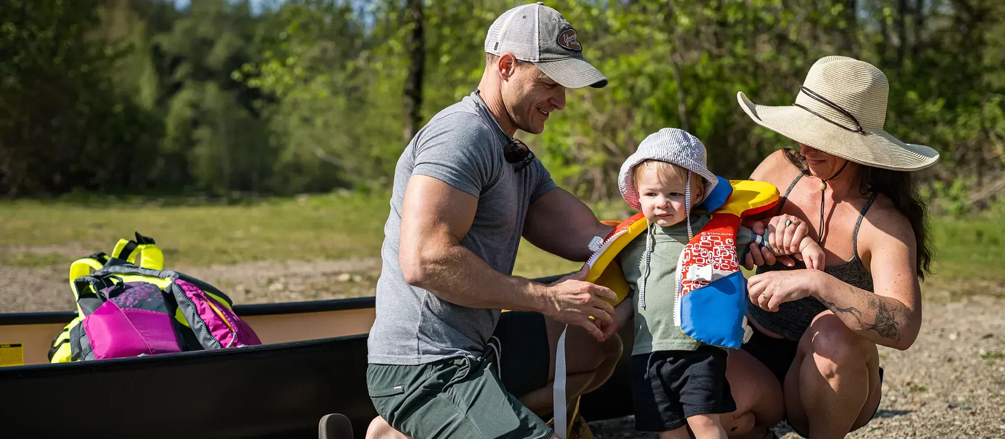 Family outdoors fitting child with Stohlquist life jacket beside kayak and paddling gear